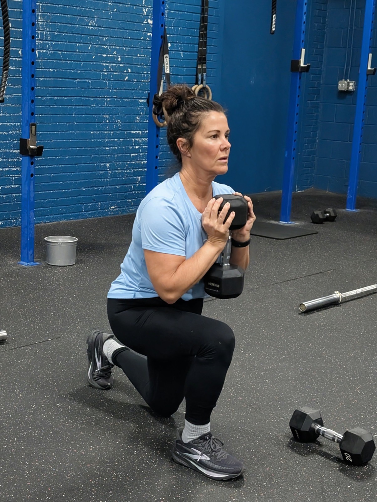 A member holding a dumbbell at the bottom of a lunge