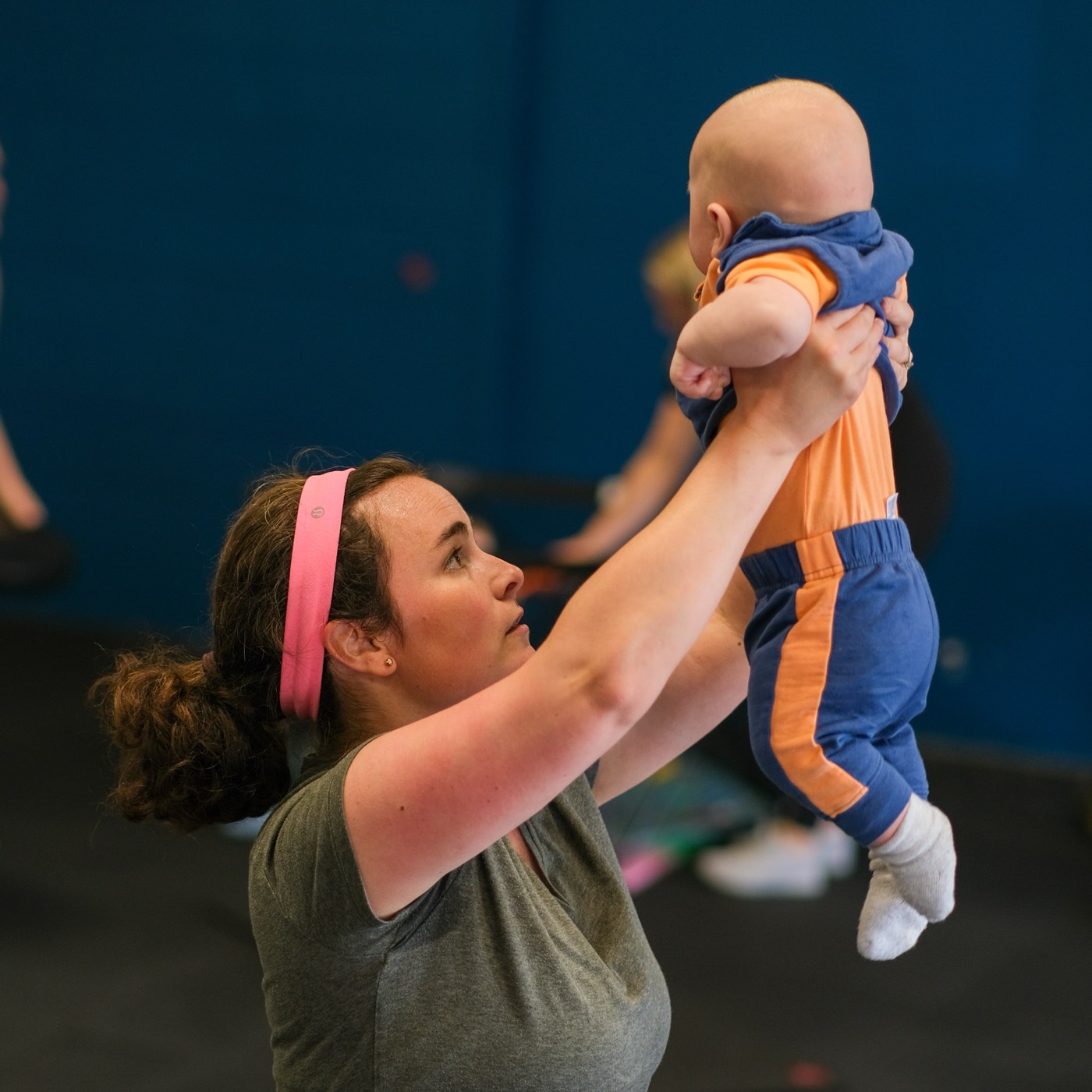 A mom lifting her baby overhead in the gym, both laughing